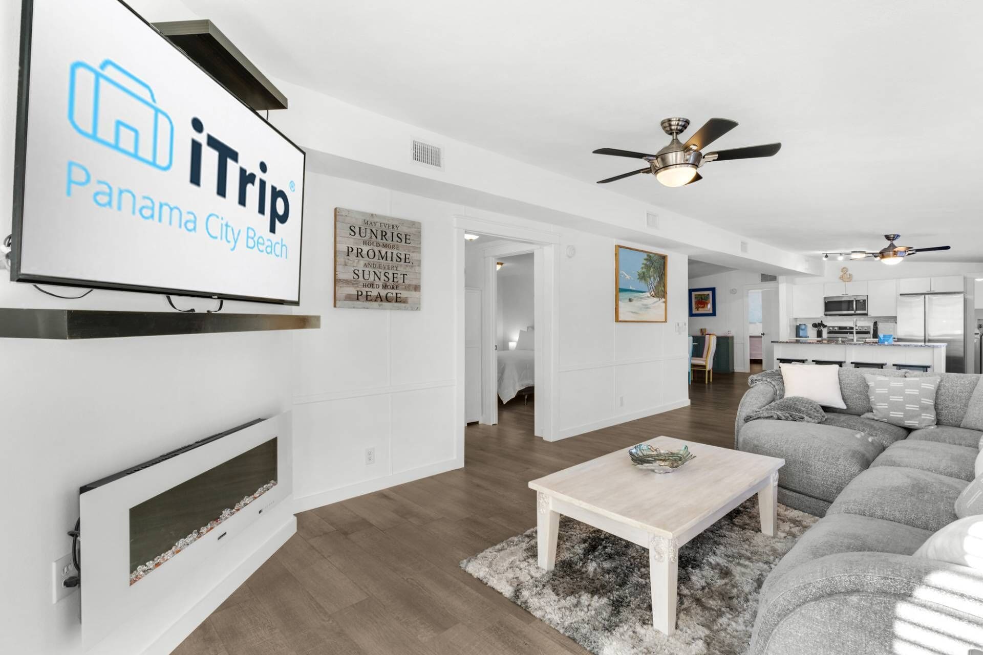 A modern living room with a fireplace, a ceiling fan, and a dining area with a light-colored table and gray sofa.