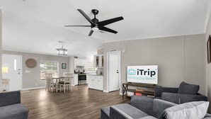 A modern living room with grey sofas, a dining area, a kitchen, and a ceiling fan. - Magic On Magnolia (Panama City Beach)