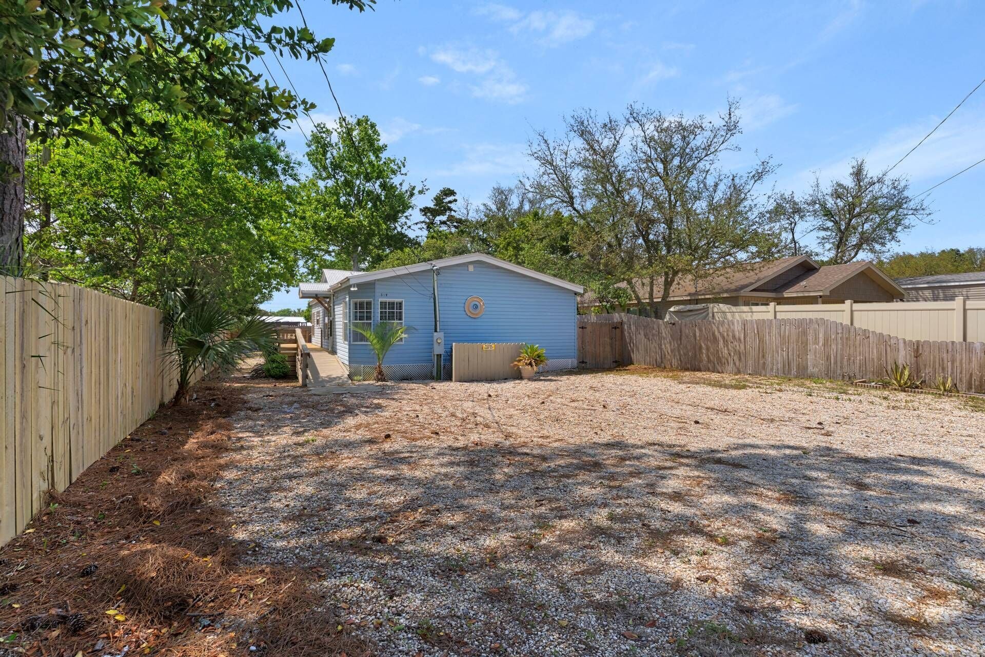 A small, single-story house with a blue exterior, surrounded by a wooden fence and trees.
