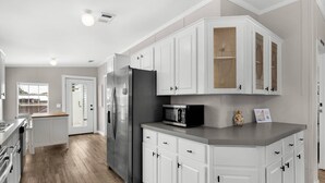 A modern kitchen with white cabinetry, a stainless steel refrigerator, and a microwave. - Magic On Magnolia (Panama City Beach)
