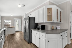 A modern kitchen with white cabinetry, a stainless steel refrigerator, and a microwave. - Magic On Magnolia (Panama City Beach)
