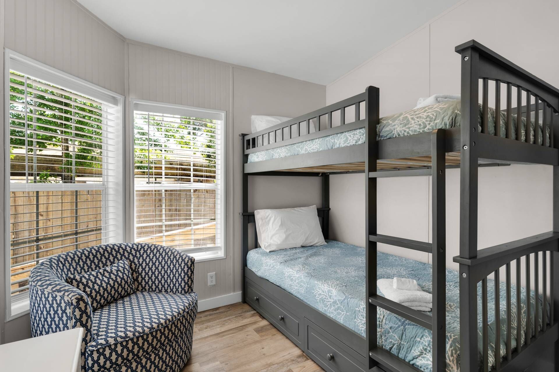 Habitación con literas, una silla estampada, ventanas amplias y vistas a zonas verdes.