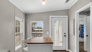 A compact kitchen with a wooden countertop, white cabinetry, and a door leading to a garage. - Magic On Magnolia (Panama City Beach)