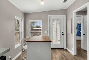 A compact kitchen with a wooden countertop, white cabinetry, and a door leading to a garage. - Magic On Magnolia (Panama City Beach)