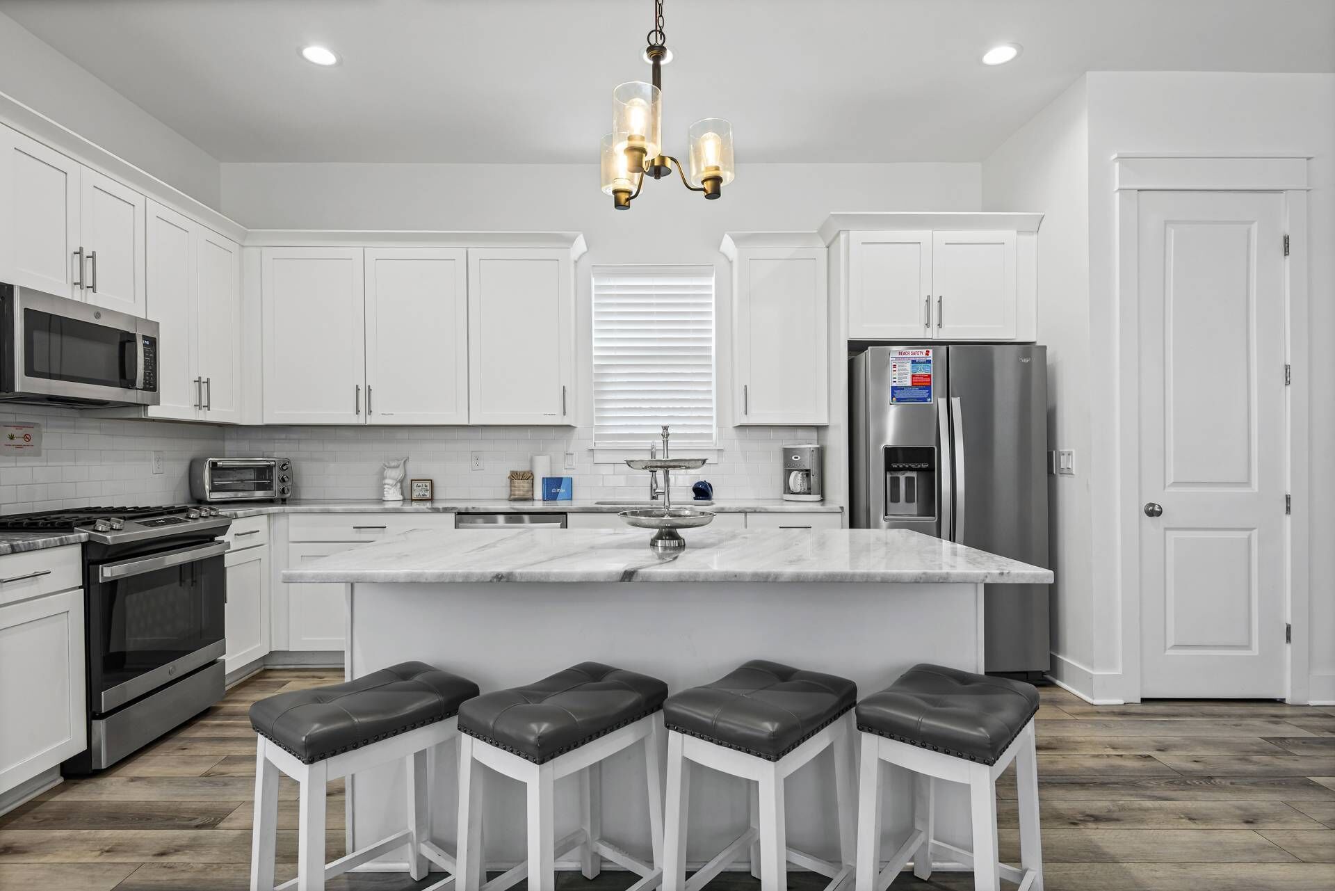 A modern kitchen with white cabinetry, a central island with bar stools, stainless steel appliances, and a chandelier.