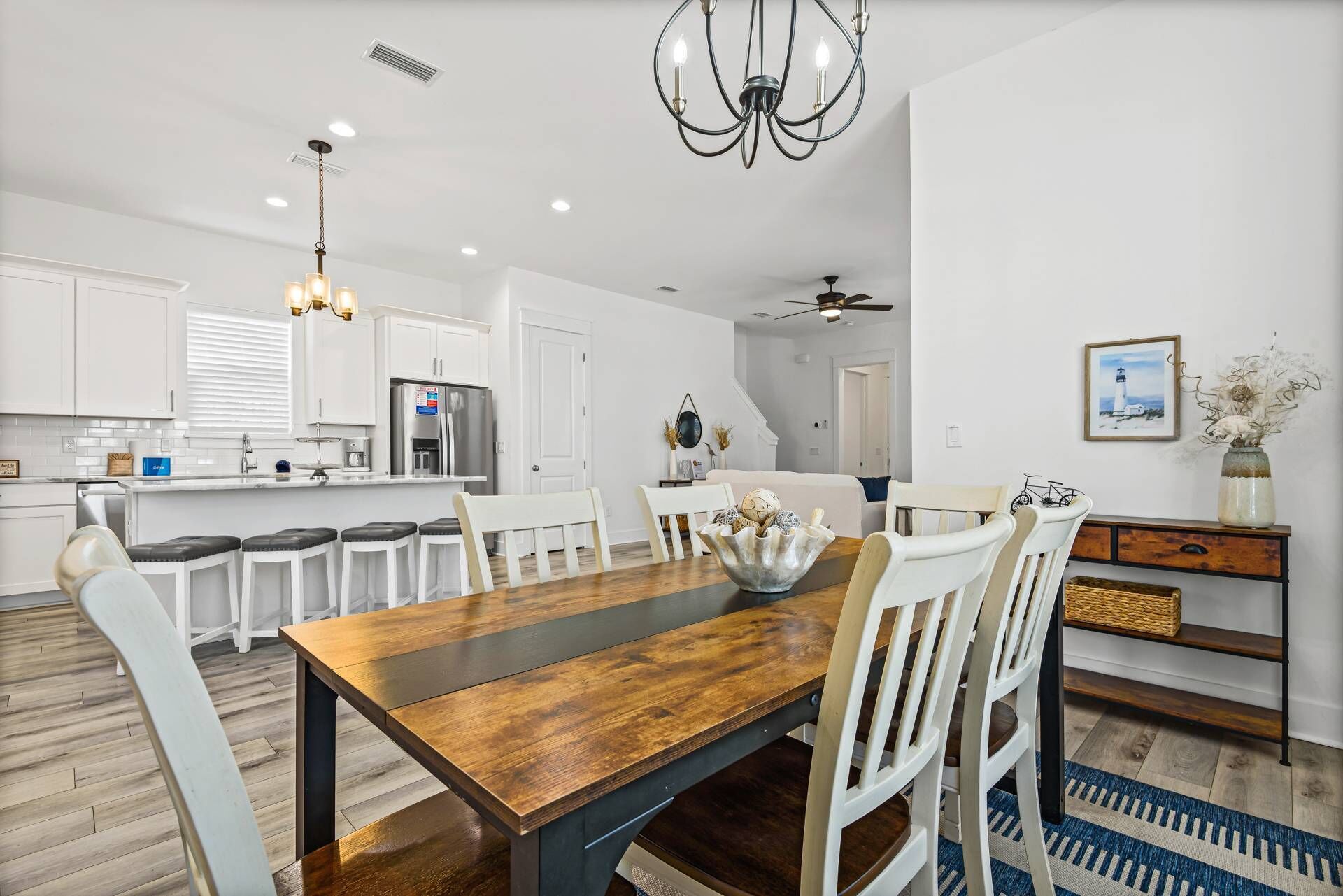A modern kitchen with white cabinets, a stainless steel refrigerator, and a dining area with a wooden table and white chairs.