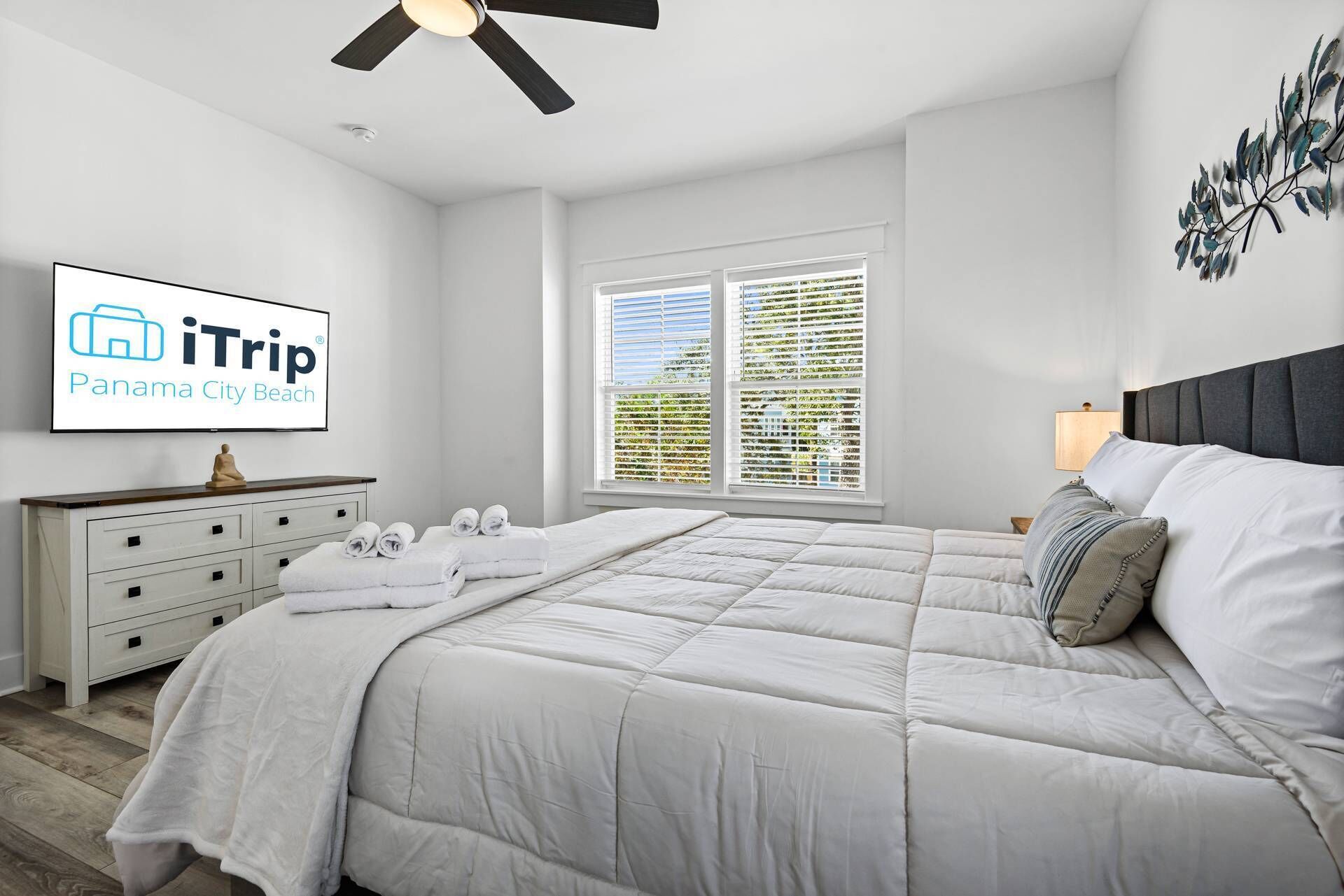 A hotel room with a bed, a nightstand, a lamp, a ceiling fan, and a window with blinds.