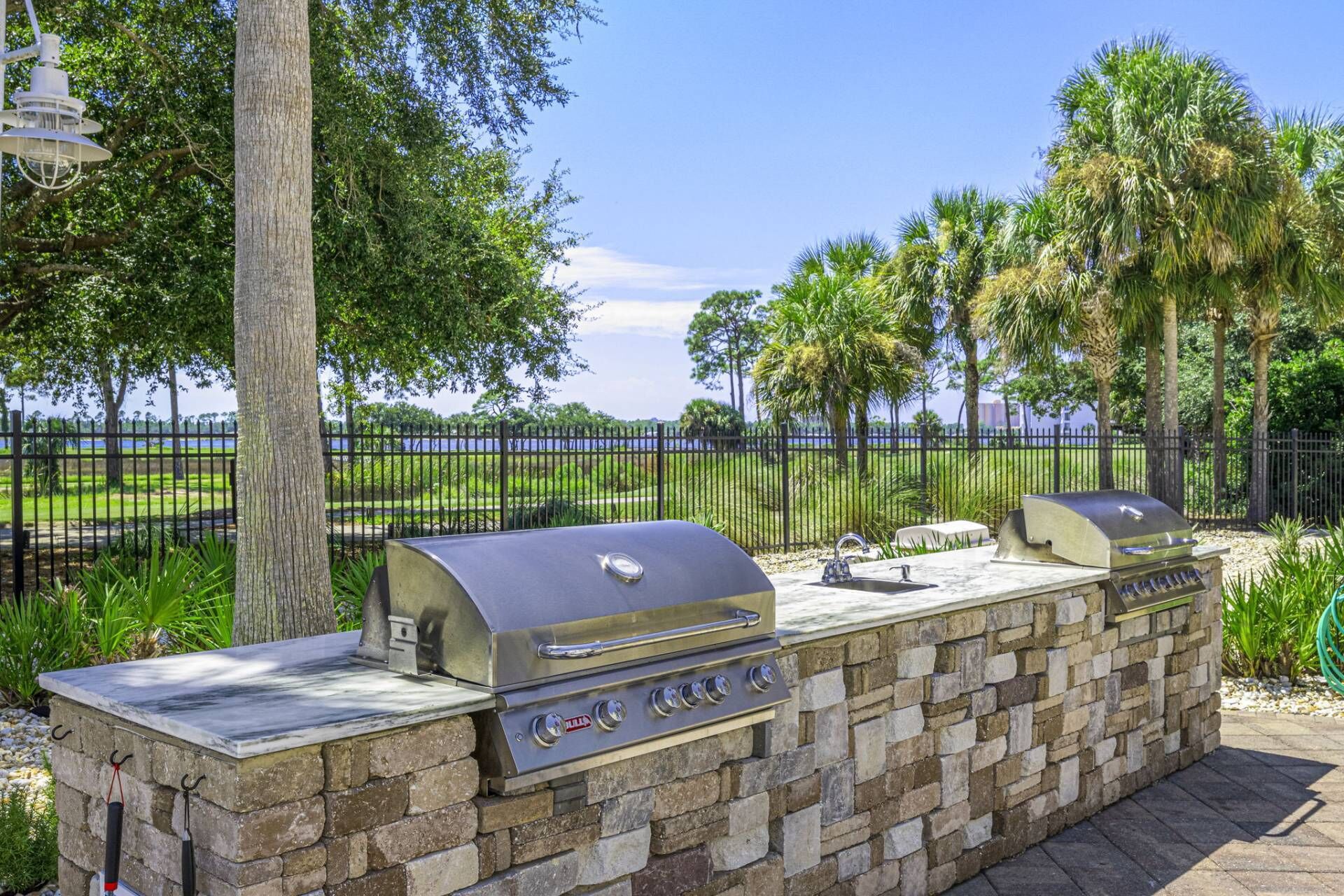An outdoor grill station with a stone wall, a metal grill, and a view of a body of water.