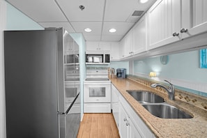 A modern kitchen with stainless steel appliances, white cabinetry, and a granite countertop. - Sunbird 204w (Panama City Beach)