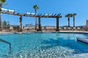 Ein klares, blaues Schwimmbecken mit einer hölzernen Pergola darüber, umgeben von Palmen und Liegestühlen.