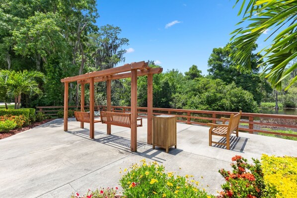 A wooden swing set with benches, a wooden planter, and a concrete deck with flower beds.