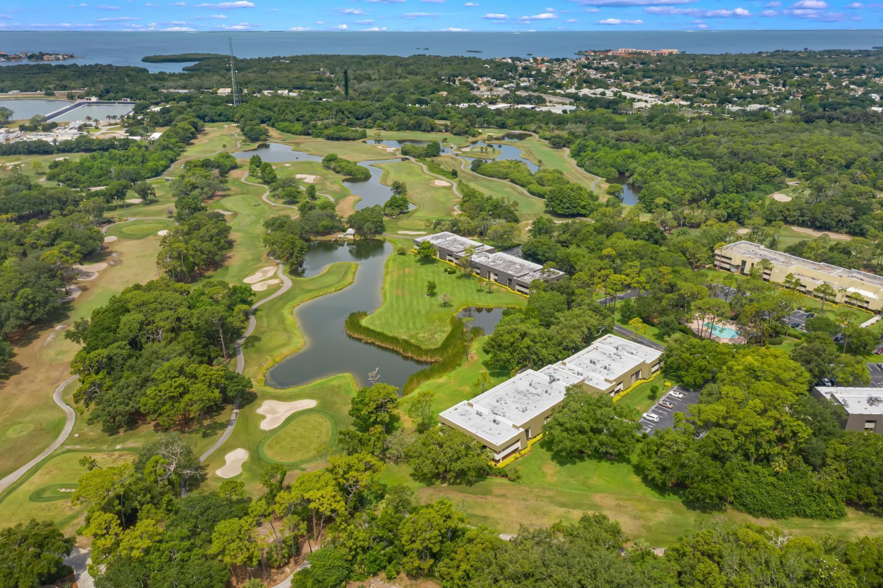 Vista aérea de um campo de golfe com várias lagoas, rodeado por vegetação densa e edifícios residenciais.