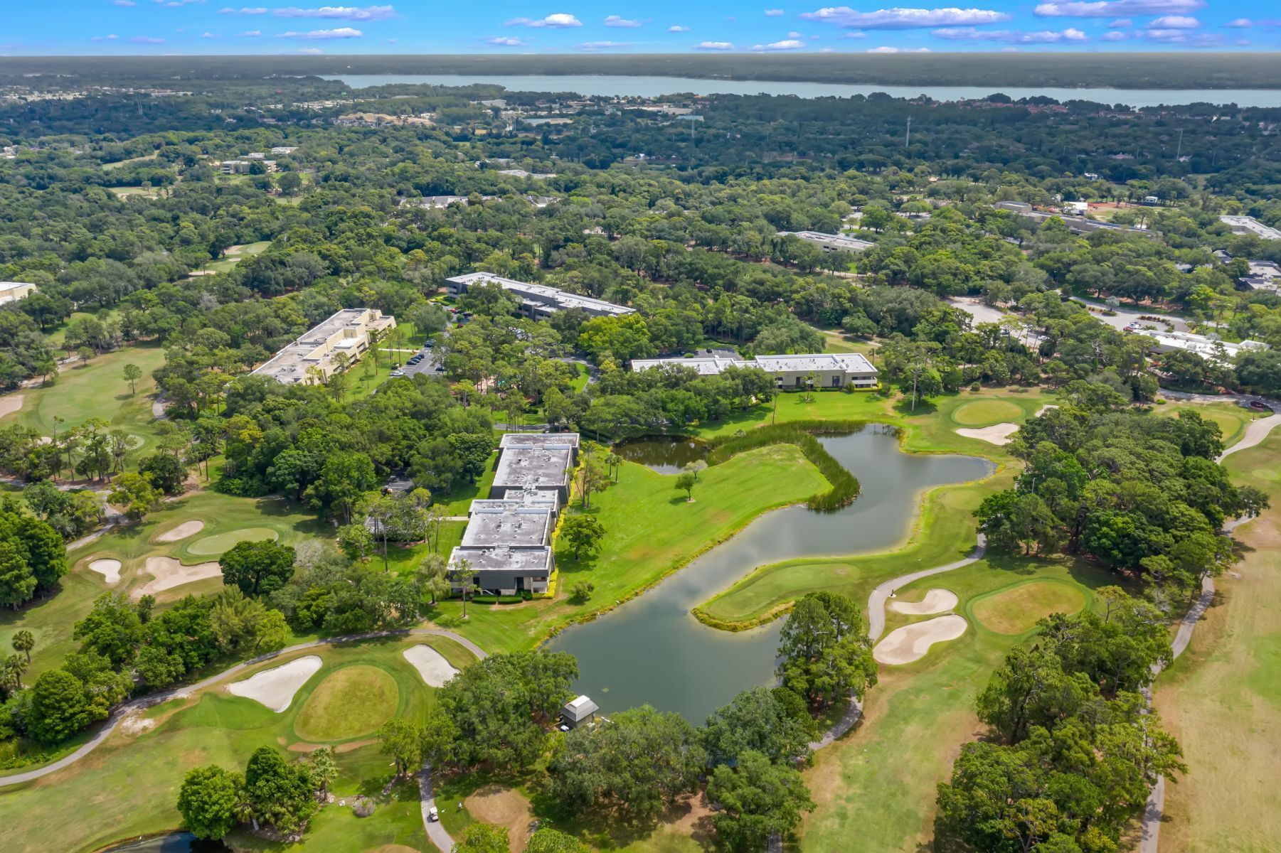 Vista aérea de un campo de golf con un estanque, rodeado de árboles frondosos y edificios.