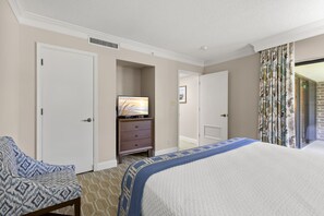 A hotel room with a bed, a TV, a dresser, and a door leading to another room.