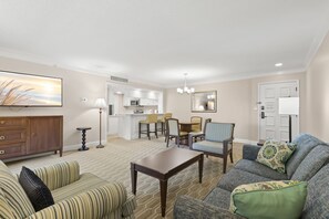 A hotel room with a living area, dining space, kitchenette, and a large mirror.