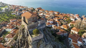 A coastal town with a prominent castle on a cliff, surrounded by houses with red-tiled roofs. - Glykofilousa Tiny Ouse (Lesvos)