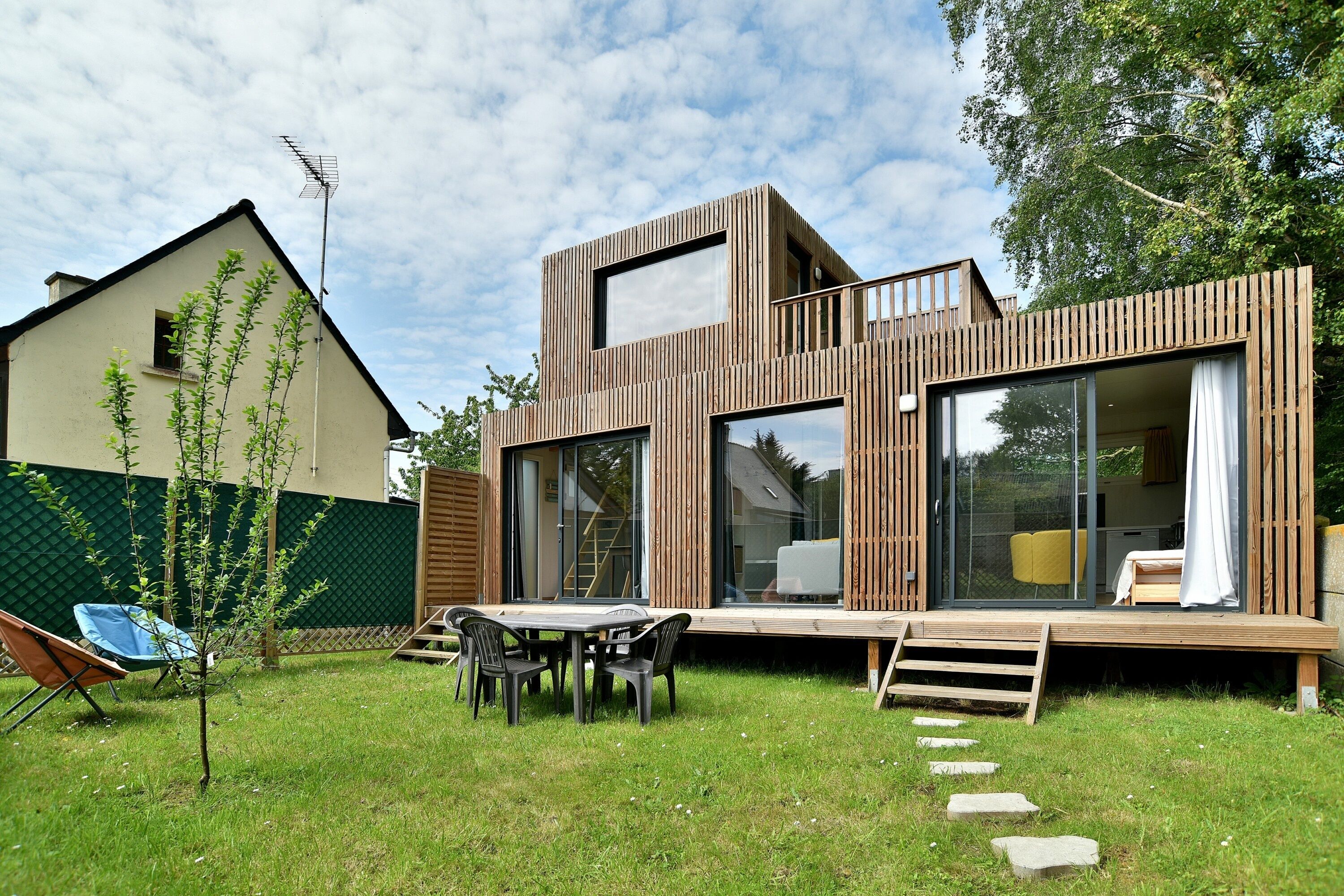 A modern house with a deck, a small garden, and a blue chair.