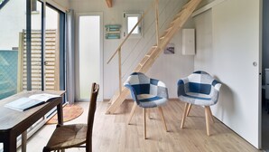 A modern interior with a wooden staircase, a dining area with a table and chairs, and a view through a glass door. - La Maison du Bord de Mer – Charmant cocon pour 4 (Saint-Jacut-de-la-Mer)