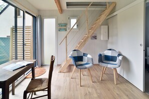 Ein modernes Interieur mit einer Holztreppe, einer Essecke mit Tisch und Stühlen sowie Blick durch eine Glastür.