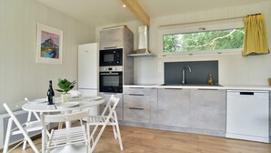 A modern kitchen with a dining area, featuring a microwave, oven, and dishwasher. - La Maison du Bord de Mer – Charmant cocon pour 4 (Saint-Jacut-de-la-Mer)