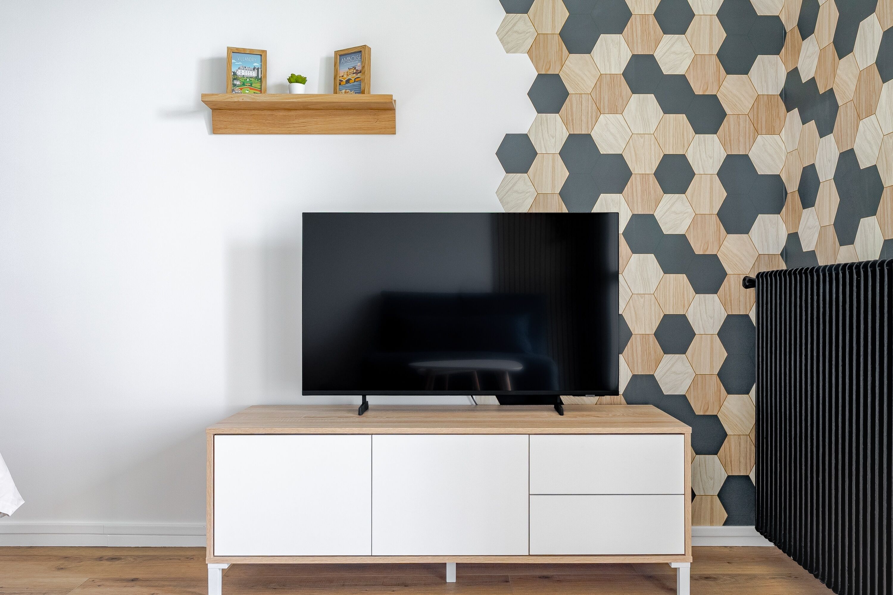 Een moderne woonkamer met een flatscreen televisie op een houten tv-meubel, een witte kast eronder en een wand met een honingraatpatroon.