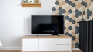 A modern living room with a flat-screen TV on a wooden TV stand, a white cabinet below, and a hexagonal patterned wall. - Bee Kaz - Beau studio à 30 min du Zoo de Beauval (Montrichard Val de Cher)