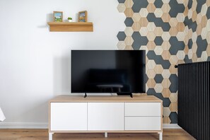 A modern living room with a flat-screen TV on a wooden TV stand, a white cabinet below, and a hexagonal patterned wall. - Bee Kaz - Beau studio à 30 min du Zoo de Beauval (Montrichard Val de Cher)
