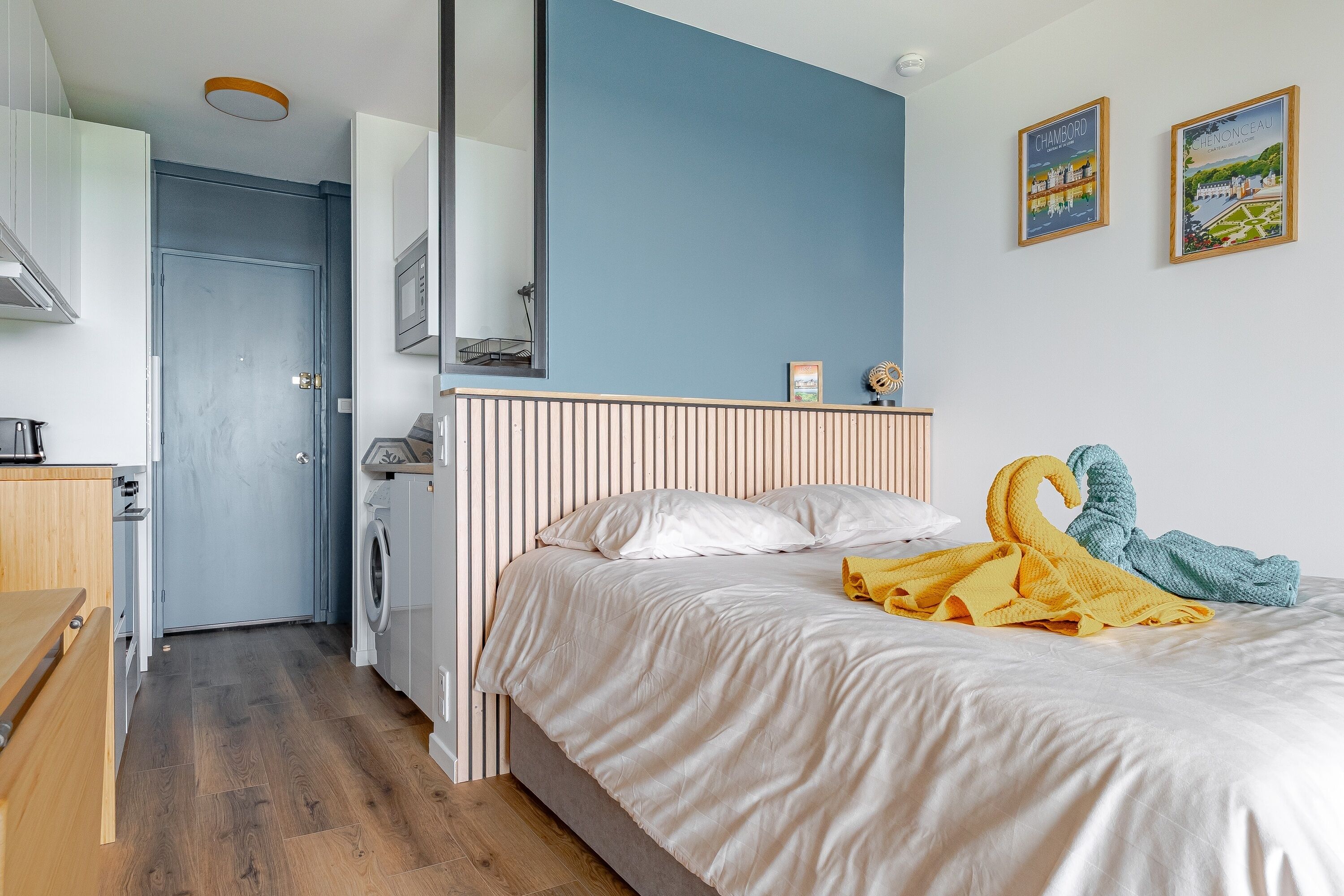 Une chambre à coucher avec un lit, un banc en bois, une machine à laver et un miroir.