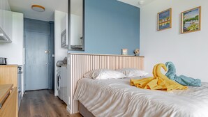 A bedroom with a bed, a wooden bench, a washing machine, and a mirror. - Bee Kaz - Beau studio à 30 min du Zoo de Beauval (Montrichard Val de Cher)