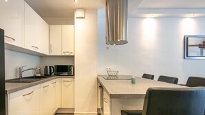Une cuisine moderne avec des meubles blancs, une hotte en acier inoxydable et un coin repas comprenant une table et des chaises.