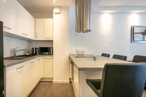 A modern kitchen with white cabinets, a stainless steel range hood, and a dining area with a table and chairs. - Le Pradel Championnet - Bel appt centre Grenoble (Grenoble)