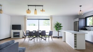 Una sala de estar moderna con un sofá, una mesa de comedor, sillas y un televisor. Cuenta con una zona de cocina con una encimera y armarios.