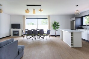 Una sala de estar moderna con un sofá, una mesa de comedor, sillas y un televisor. Cuenta con una zona de cocina con una encimera y armarios.