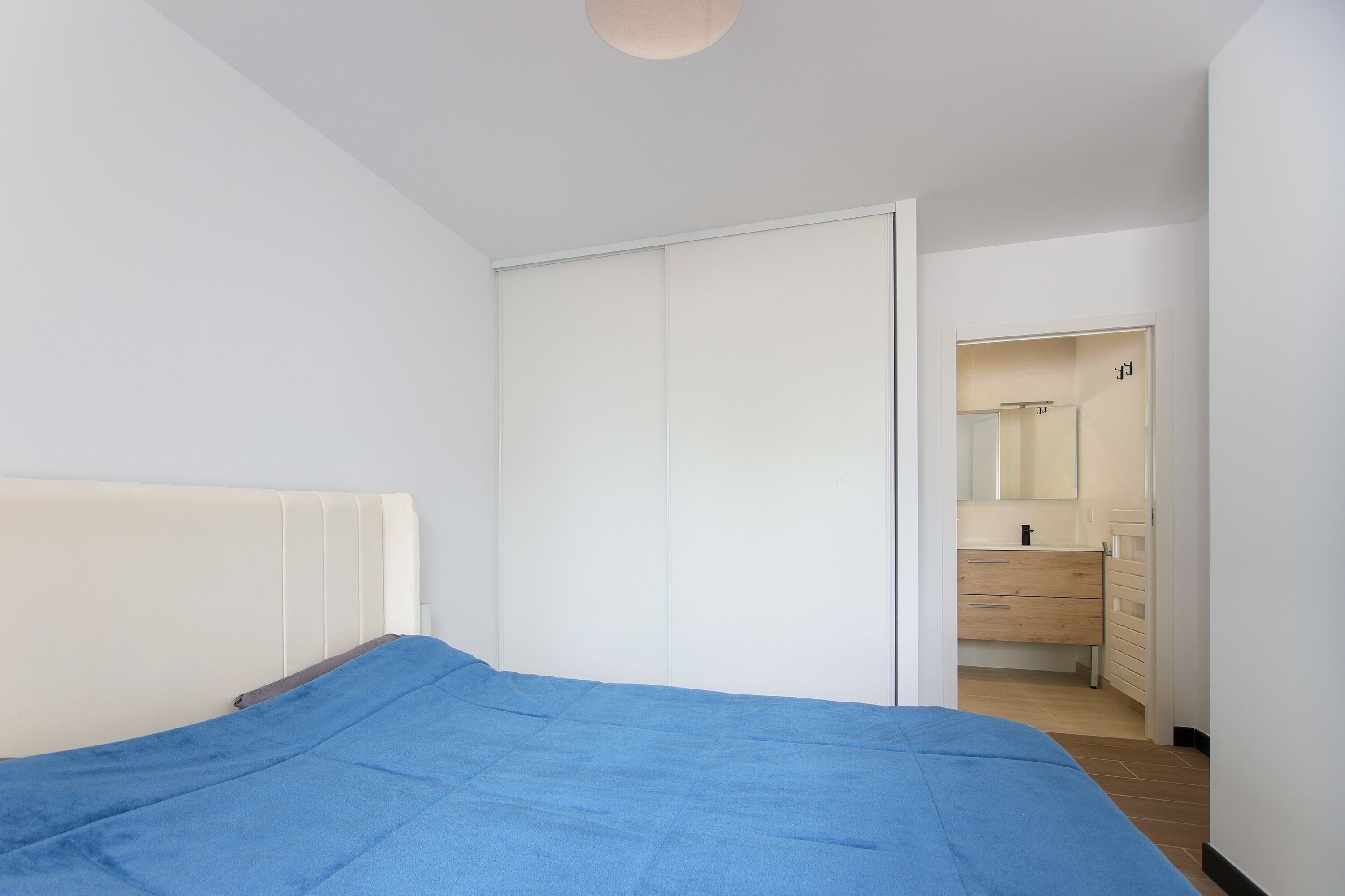 A bedroom with a bed, a wardrobe, and a bathroom visible through an open door.