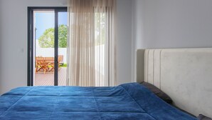 Un dormitorio con cama, ventana con cortinas y vista a un patio exterior.