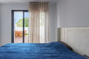 Un dormitorio con cama, ventana con cortinas y vista a un patio exterior.