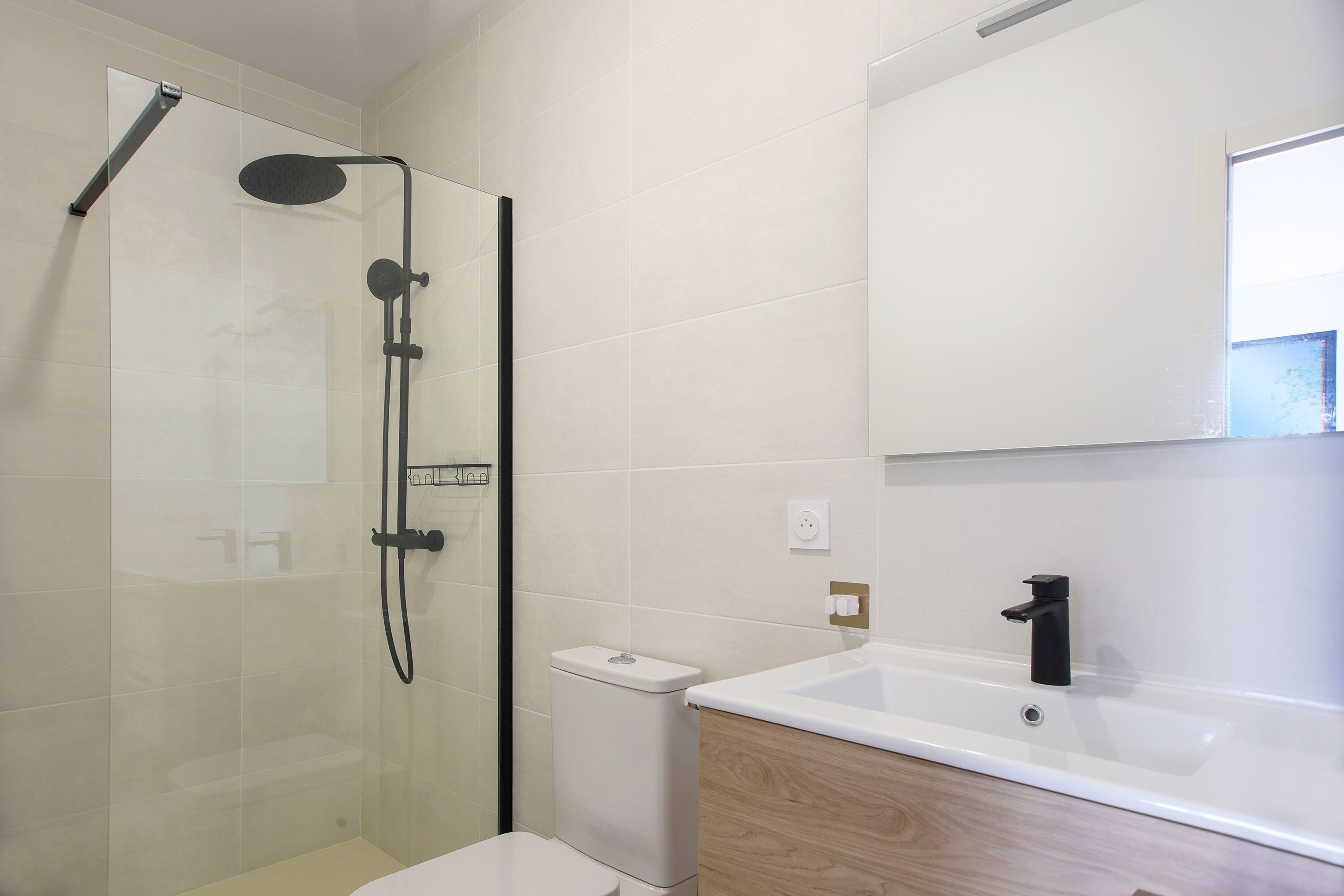 A modern bathroom with a glass shower enclosure, a white toilet, a sink with a black faucet, and a mirror above the sink.