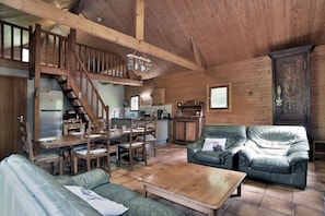 L’intérieur d’un chalet rustique comprend un coin repas, un canapé, une table basse, un escalier et une cuisine.