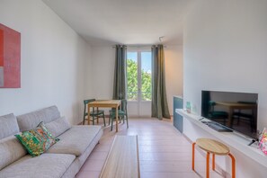 A living room with a sofa, a TV, a dining table with chairs, and a window with curtains. - La Rose de Bordeaux - Au cœur des Chartrons (Bordeaux)