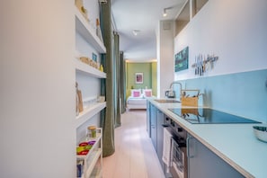 A narrow kitchen with a central island, white cabinets, and a view into a bedroom. - La Rose de Bordeaux - Au cœur des Chartrons (Bordeaux)