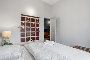 A bedroom with a bed, a nightstand with a lamp, a wall-mounted wooden hanger board, and a door leading to another room. - Le Cocon de Béziers - Au cœur du centre-ville (Béziers)