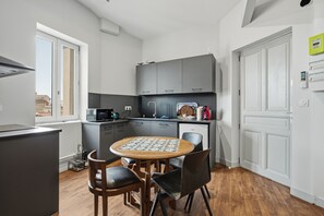 A compact kitchen with a dining table, chairs, and a microwave. - Le Cocon de Béziers - Au cœur du centre-ville (Béziers)
