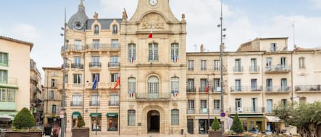 Un bâtiment historique doté d’une tour horlogée, de plusieurs drapeaux et d’une entrée principale.