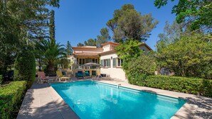 Piscina com espreguiçadeiras, um alpendre coberto e uma casa com telhado em cerâmica.