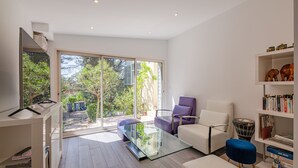 Uma sala de estar moderna com uma mesa de centro de vidro, um sofá branco, uma poltrona roxa e uma estante.