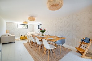 Ein moderner Essbereich mit einem Holztisch, weißen Stühlen und einer gewebten Deckenleuchte.
