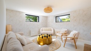 Ein modernes Wohnzimmer mit einem runden Couchtisch aus Gold, weißen Sofas und einem weißen Sessel.