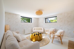 Ein modernes Wohnzimmer mit einem runden Couchtisch aus Gold, weißen Sofas und einem weißen Sessel.