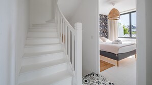Eine Treppe führt zu einem Schlafzimmer mit einem Bett, einer Hängeleuchte und Blick durch eine offene Tür.