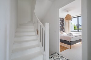 Eine Treppe führt zu einem Schlafzimmer mit einem Bett, einer Hängeleuchte und Blick durch eine offene Tür.
